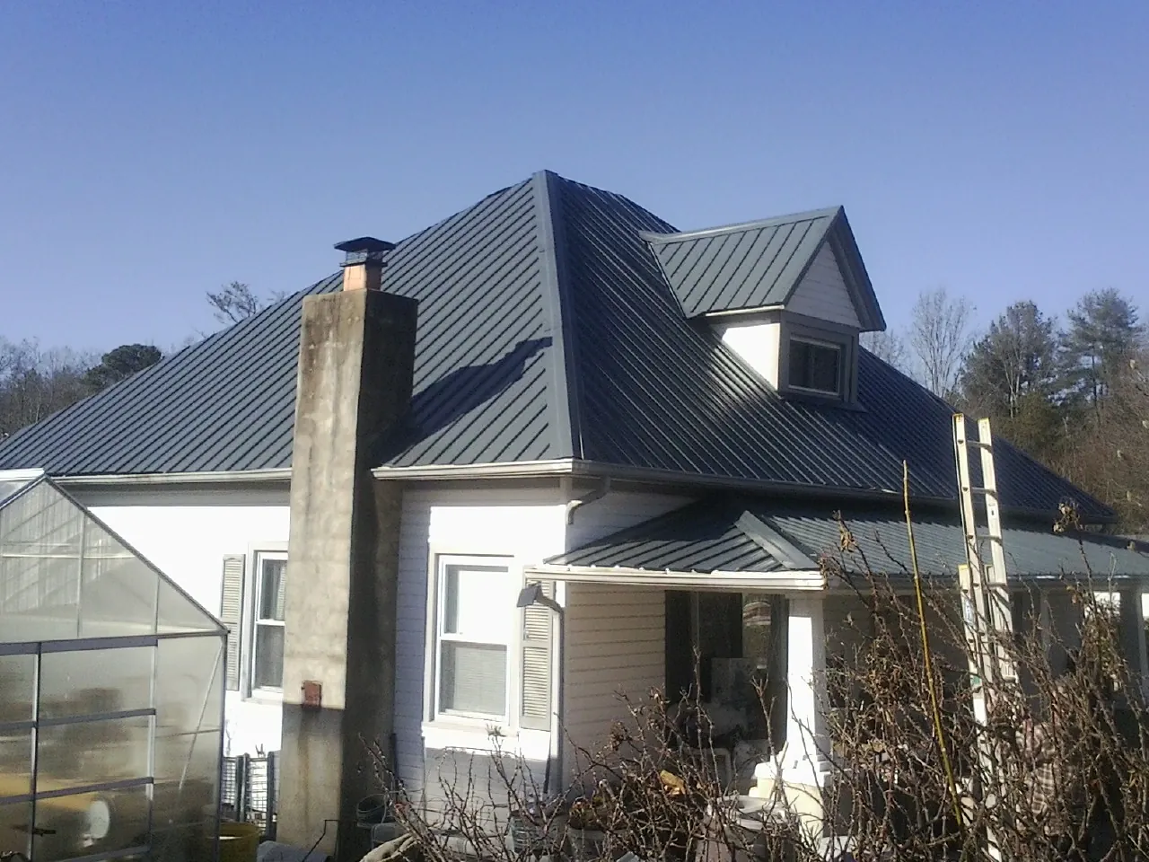 Dark blue standing seam metal roof on a white farmhouse with dormer — Slate & Tile Roof Repair by Roofing Brothers in Bostic