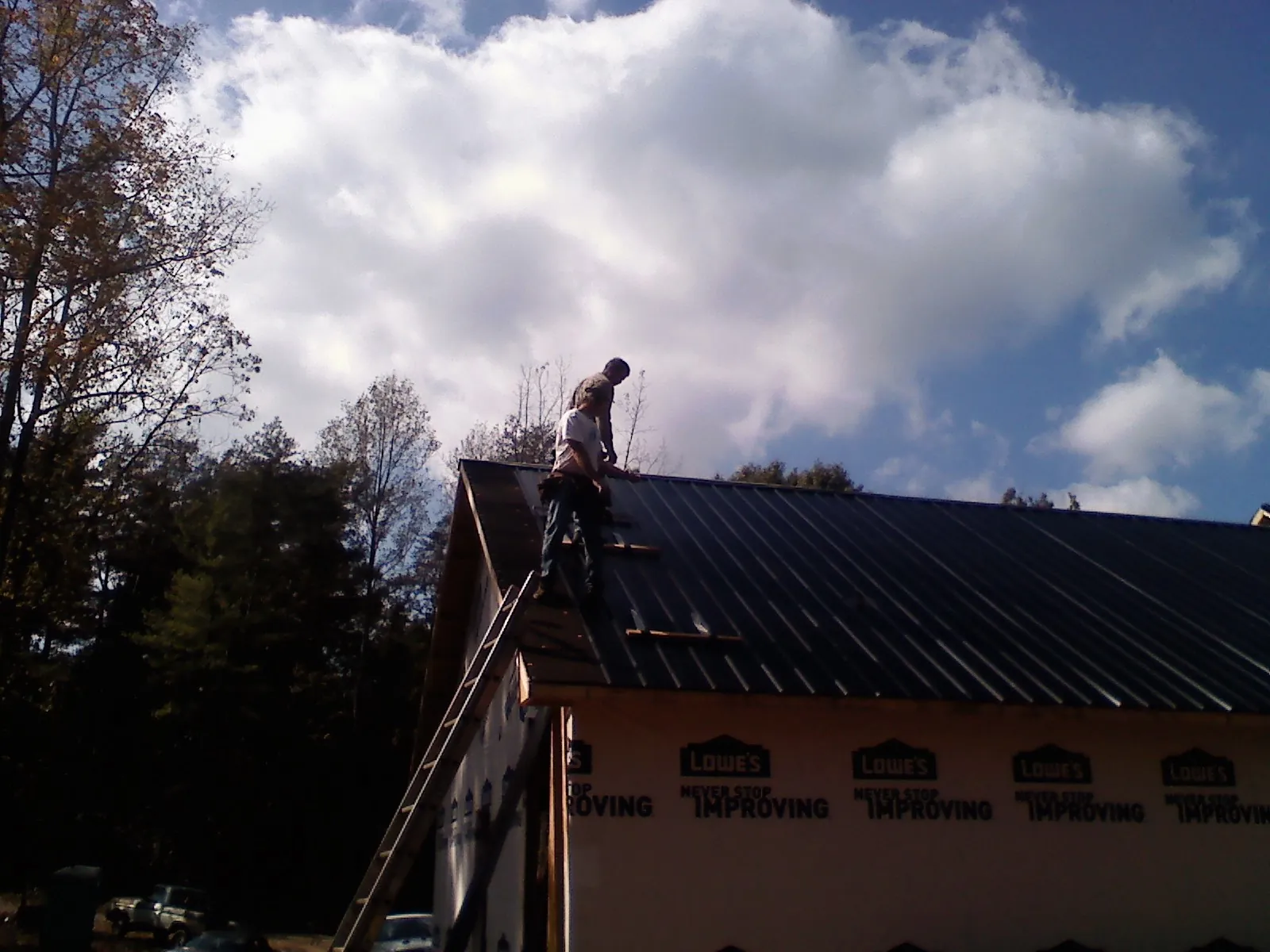 Roofer fastening dark metal panels high against a cloudy sky, from a Roof Inspection job in Bostic