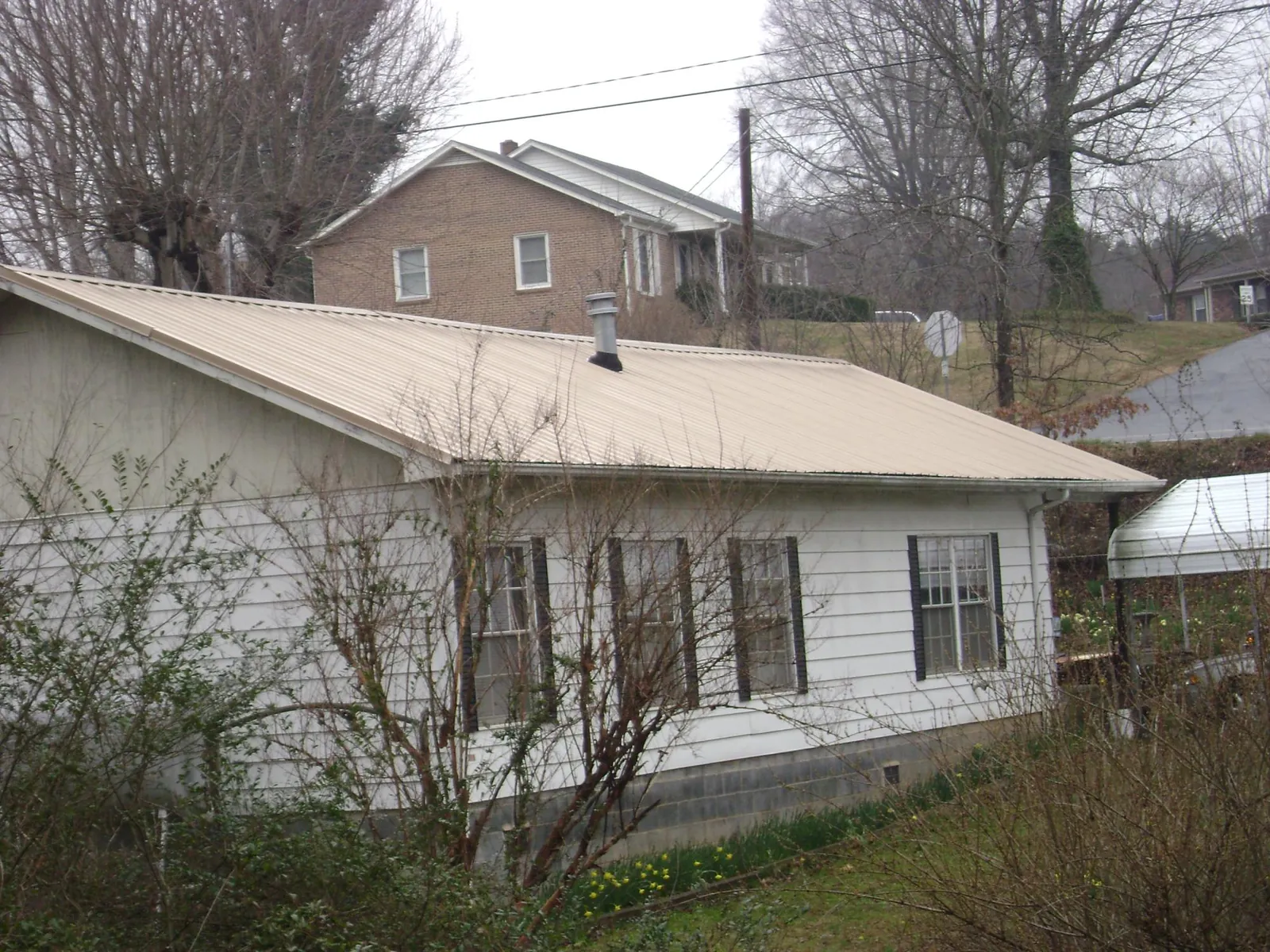 Tan metal roof on a white sided house set into a hillside — Commercial Roofing by Roofing Brothers in Bostic